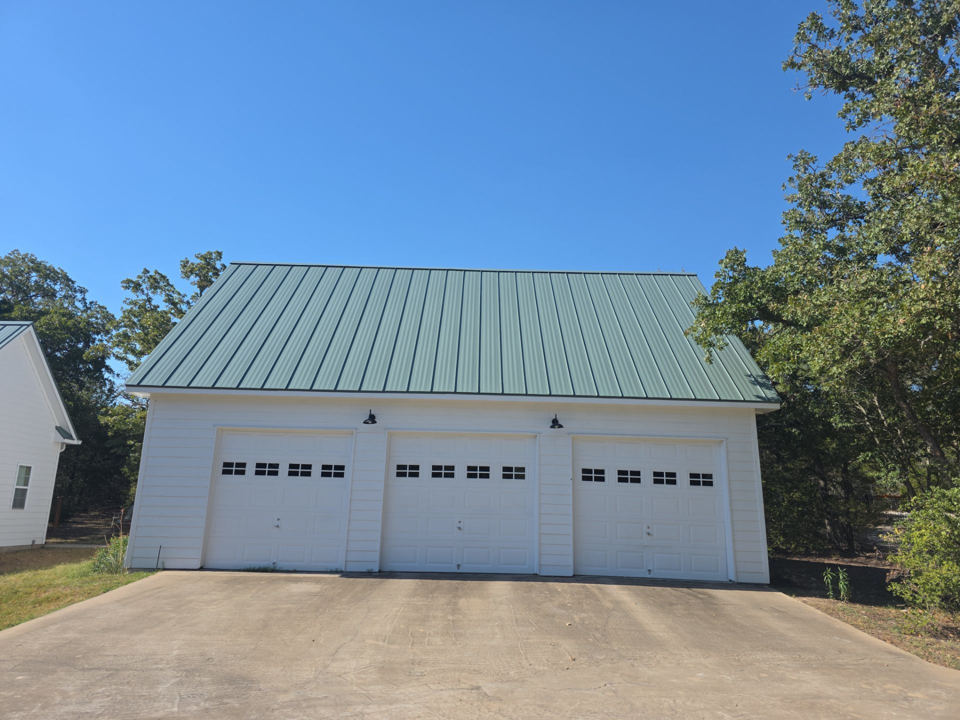 White garage with three doors, green metal roof, blue sky.