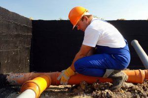 A man wearing a hard hat is kneeling on a pile of pipes.
