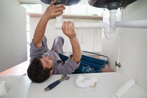 A plumber is fixing a sink pipe in a kitchen.