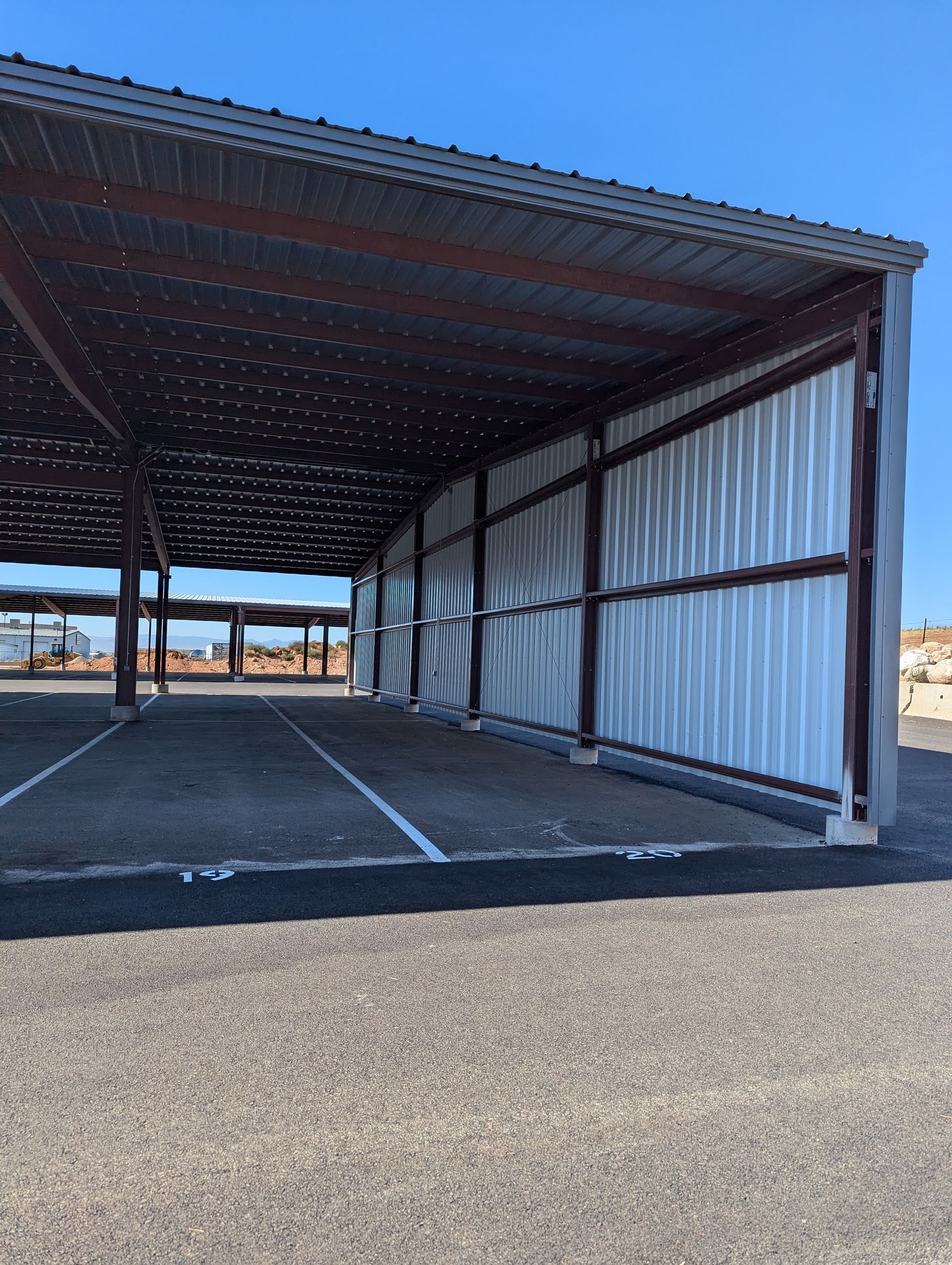 A large metal building with a roof over a parking lot.