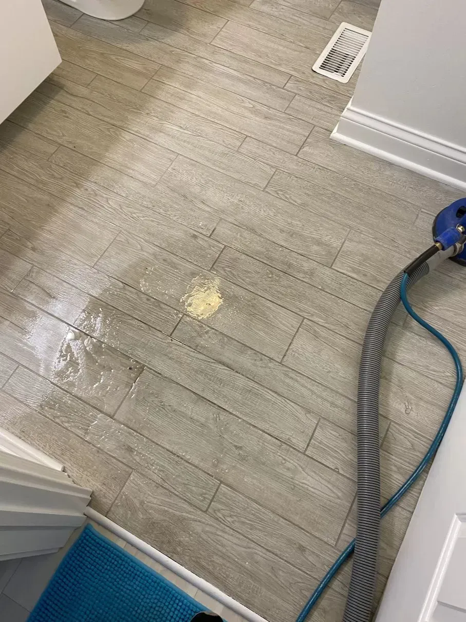 Bathroom floor being cleaned; a yellow stain and water puddles are visible. A vacuum hose is in view.
