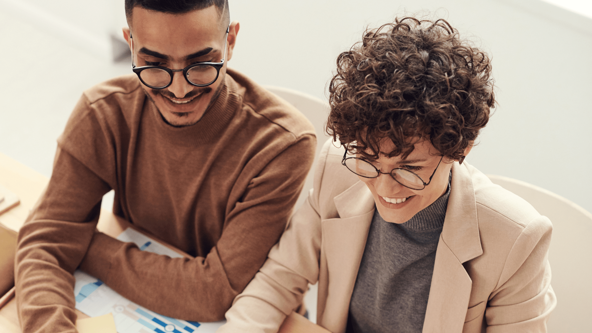 A man and a woman are sitting at a table looking at a laptop.