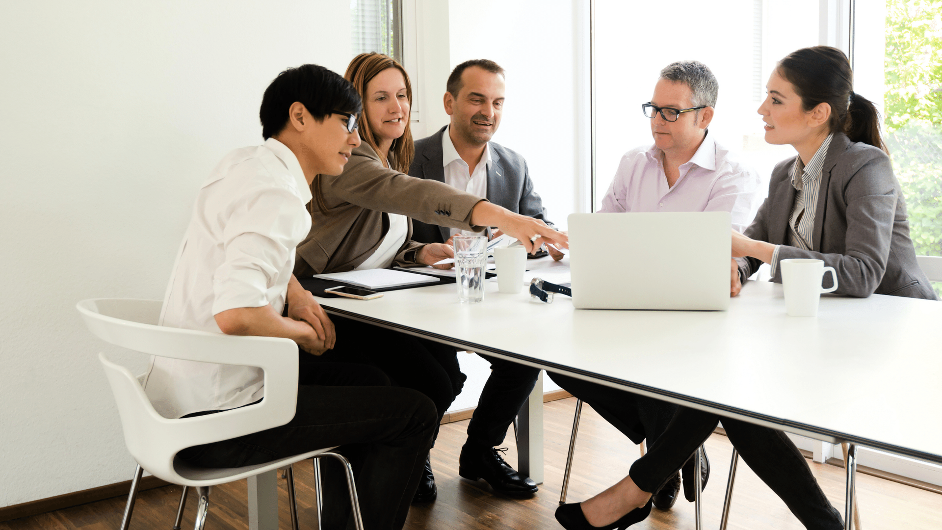 A group of people are sitting around a table with a laptop.