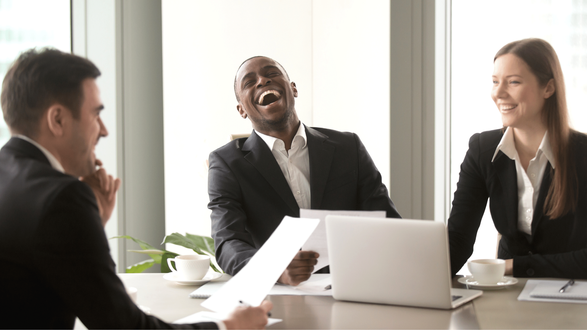 A group of business people are sitting around a table laughing.