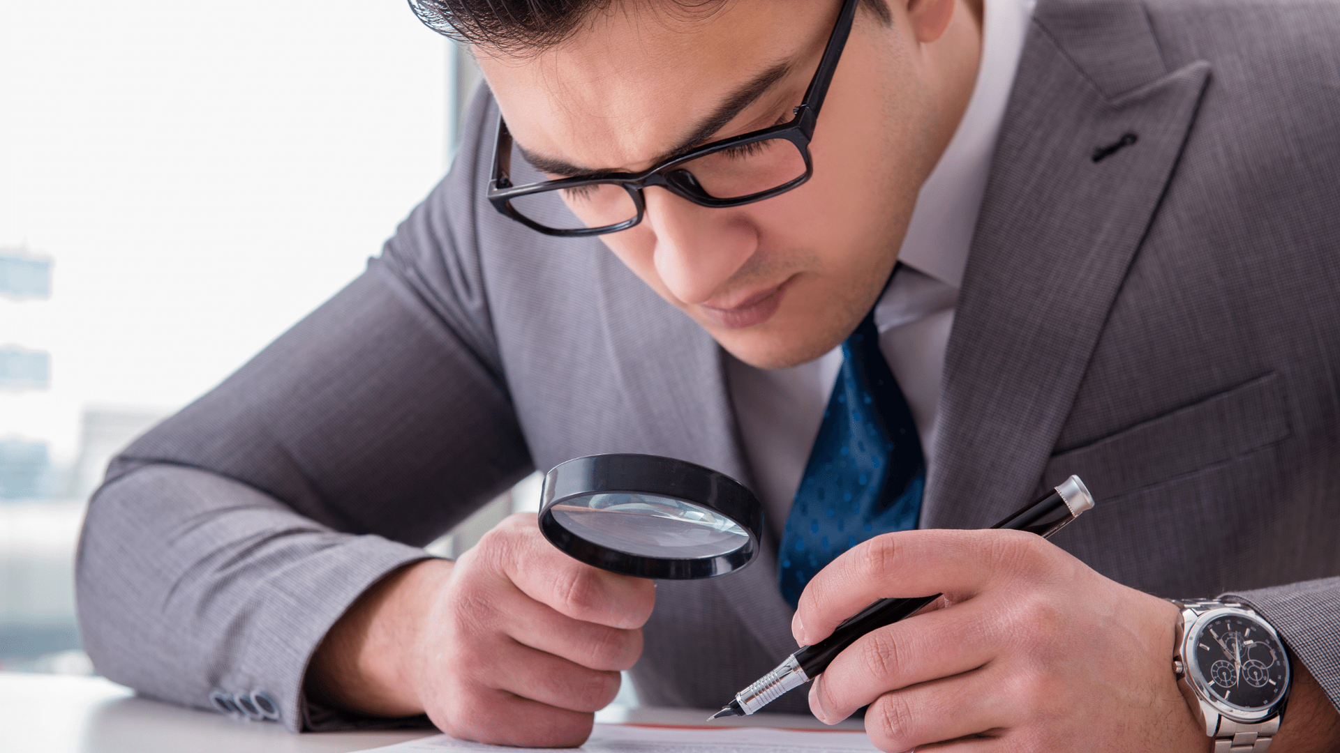 A man in a suit is looking through a magnifying glass at a piece of paper.