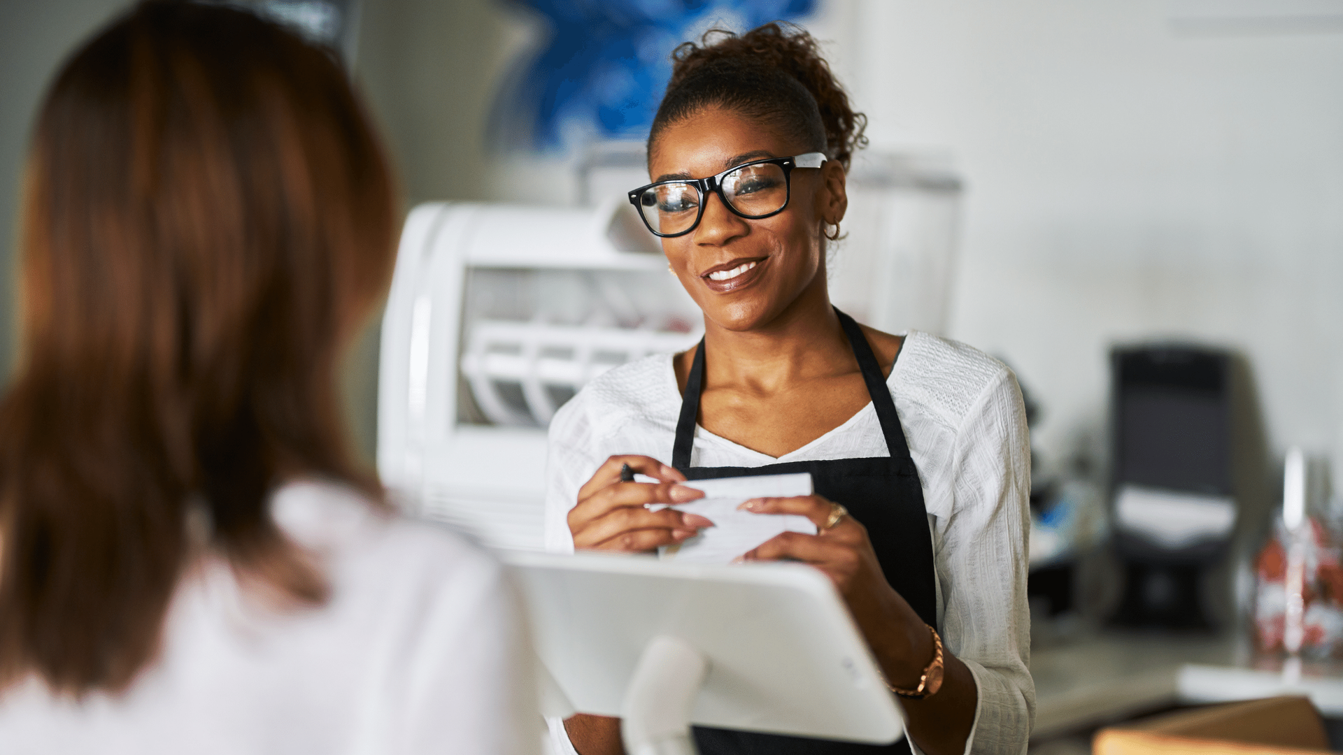 A woman is taking a order from a customer at a restaurant.