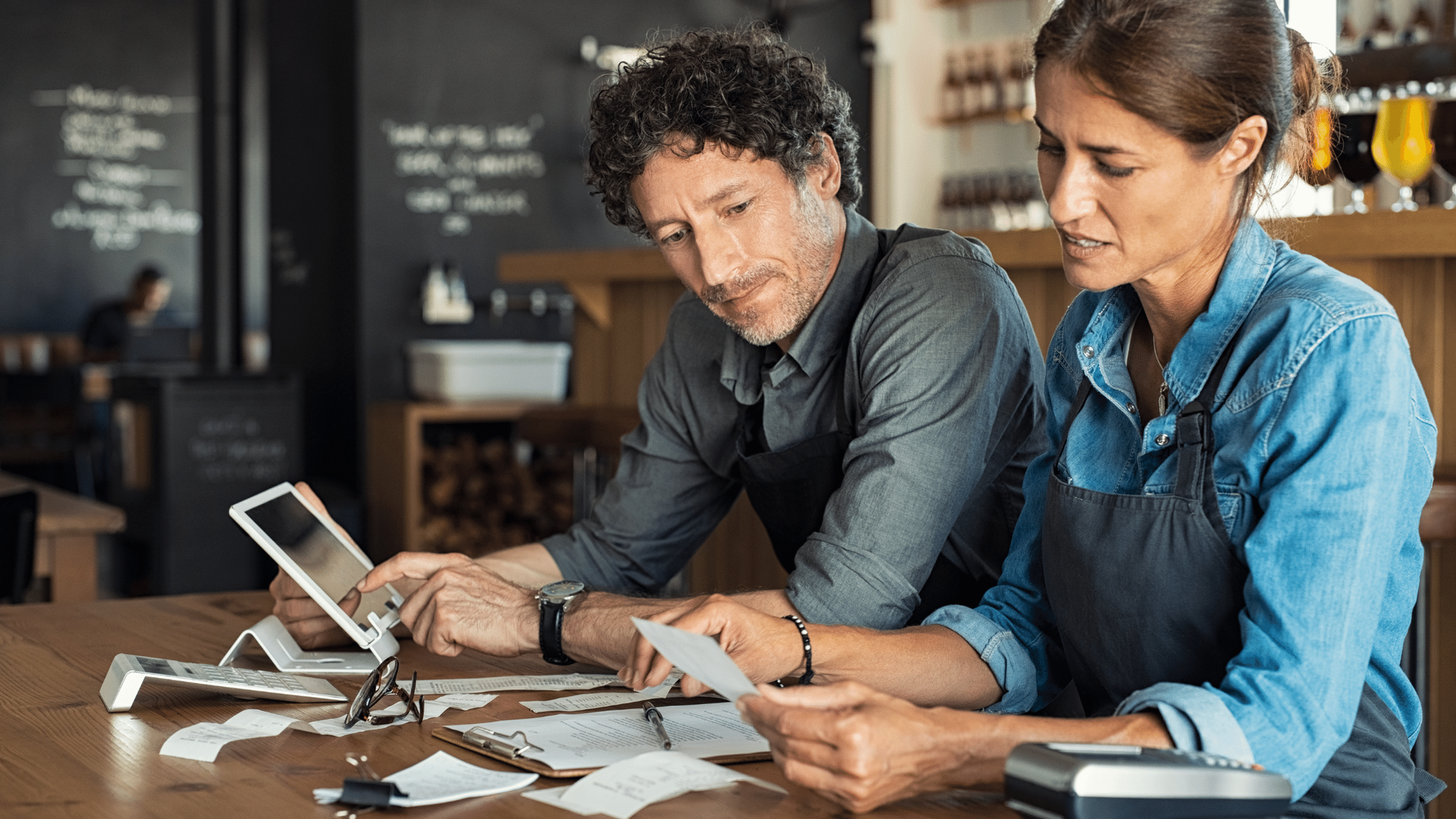 A man and a woman are sitting at a table in a restaurant looking at a tablet.