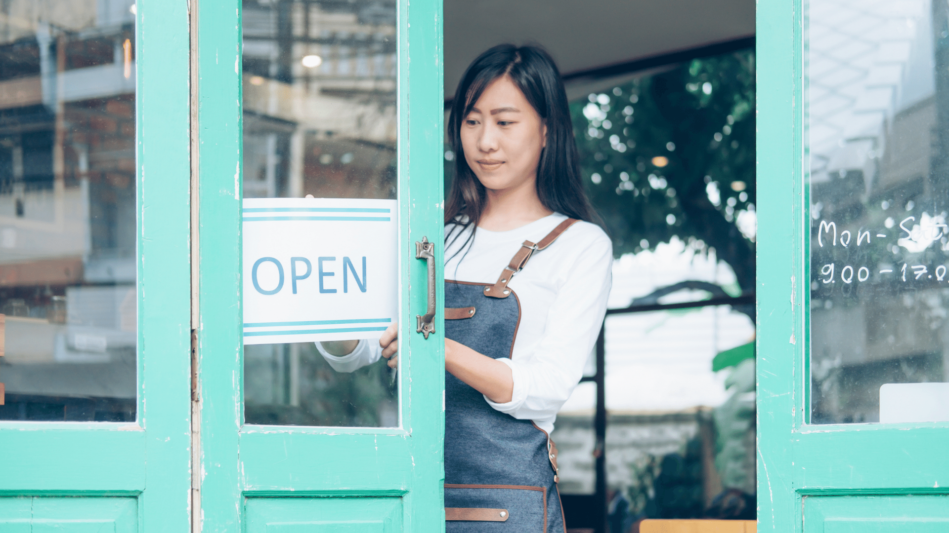 A woman is holding an open sign in front of a store door.