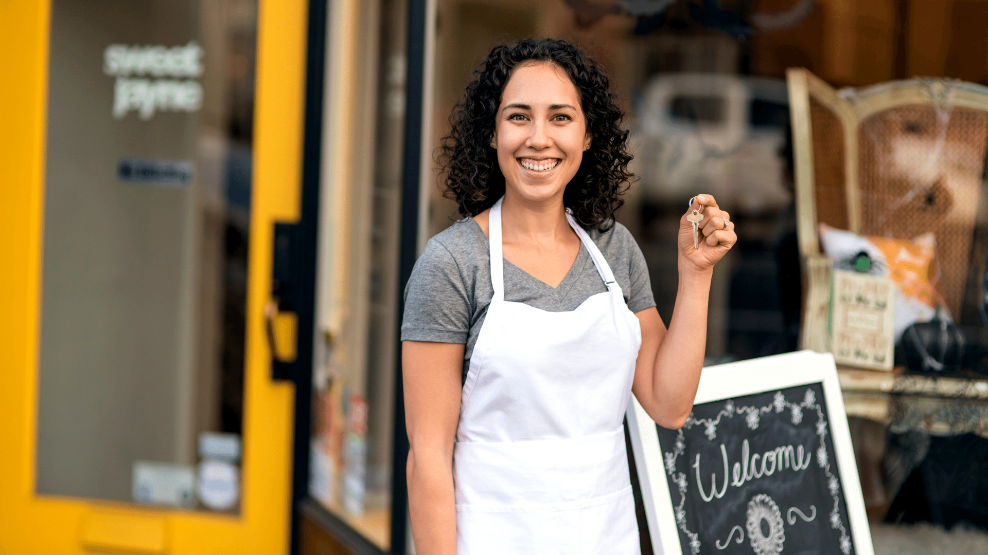 A woman in an apron is standing in front of a store holding a sign.