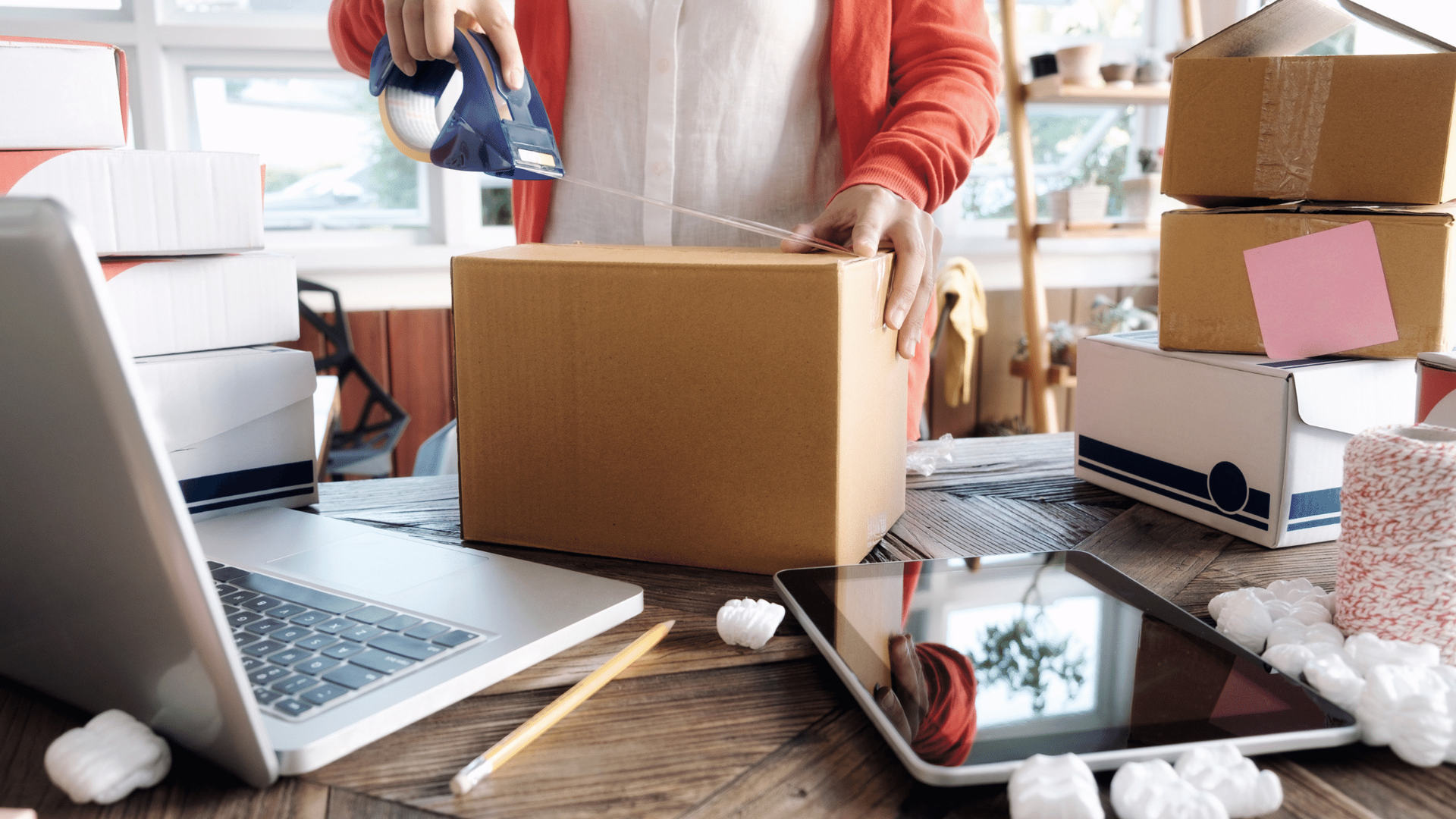 A woman is wrapping a cardboard box on a wooden table.