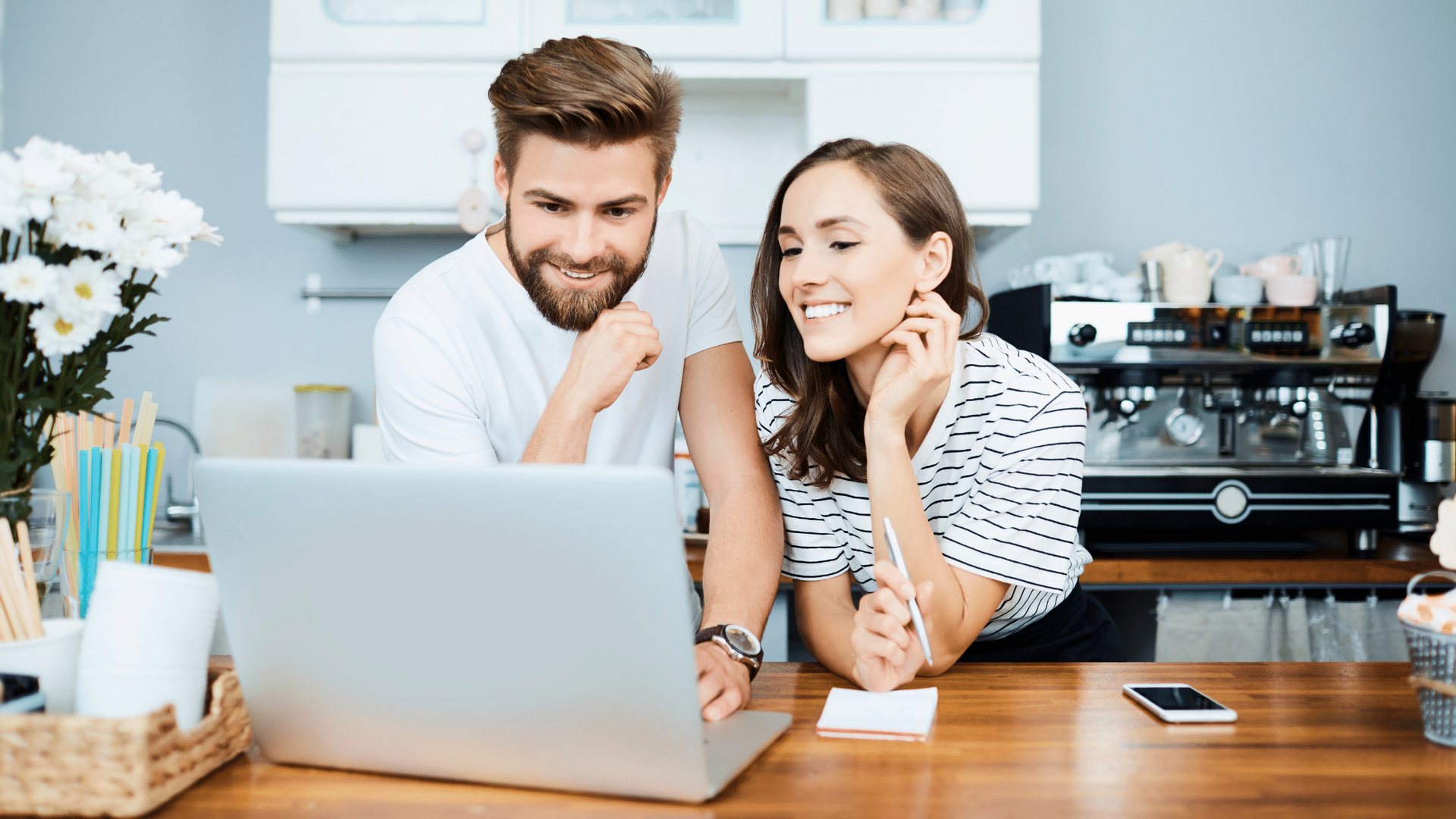 A man and a woman are sitting at a table looking at a laptop computer.