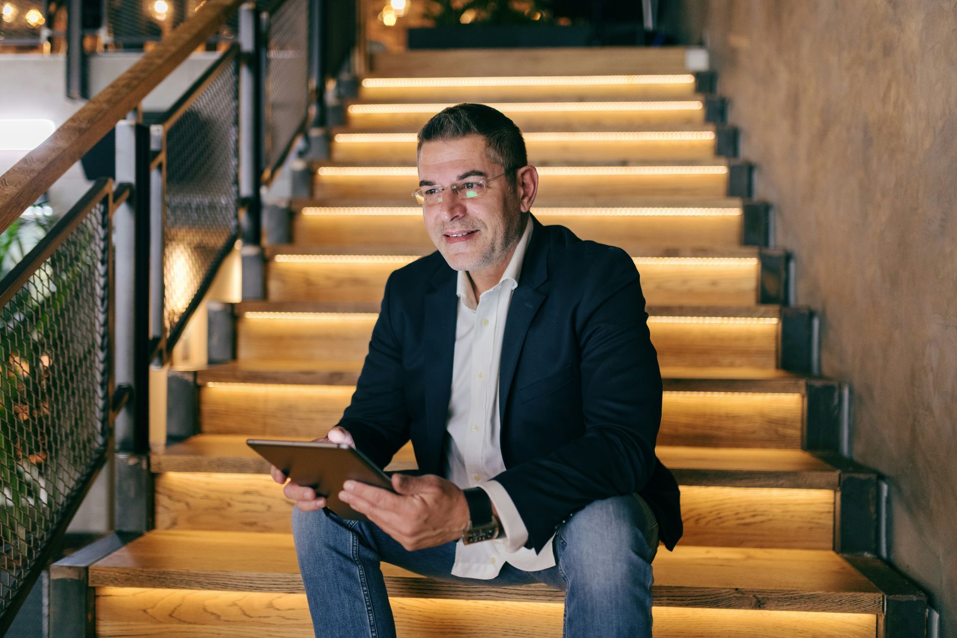 A man is sitting on a set of stairs holding a tablet.