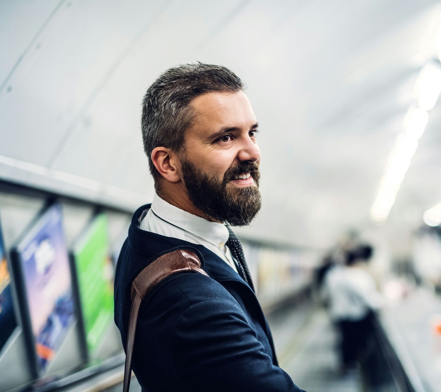 A man with a beard is standing on an escalator in a subway station.