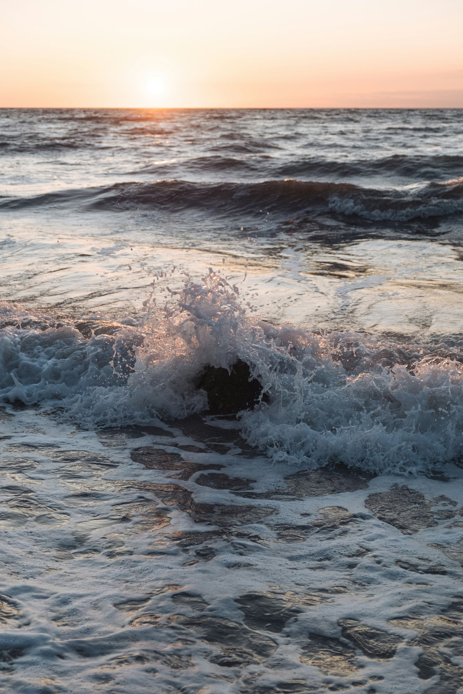 The sun is setting over the ocean and the waves are crashing on the beach.