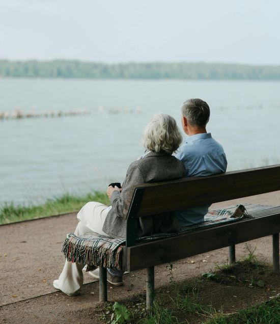 A man and a woman are sitting on a bench looking at the water.