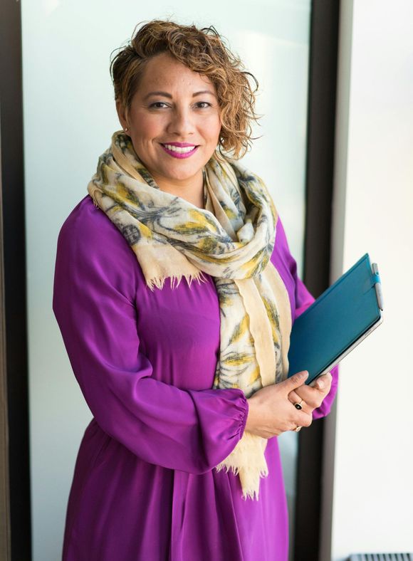 A woman in a purple dress and scarf is holding a blue folder.