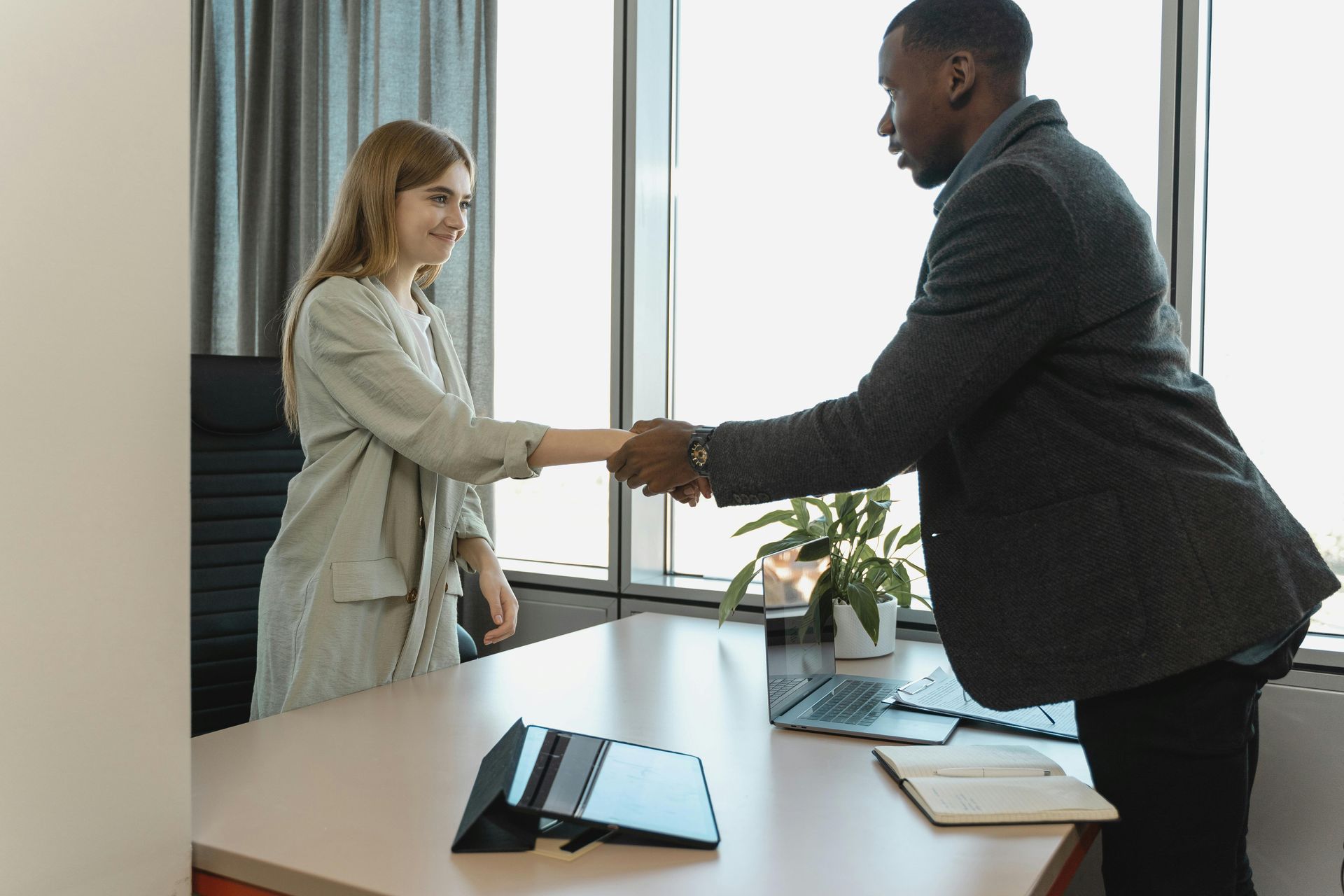 A man and a woman are shaking hands in an office.