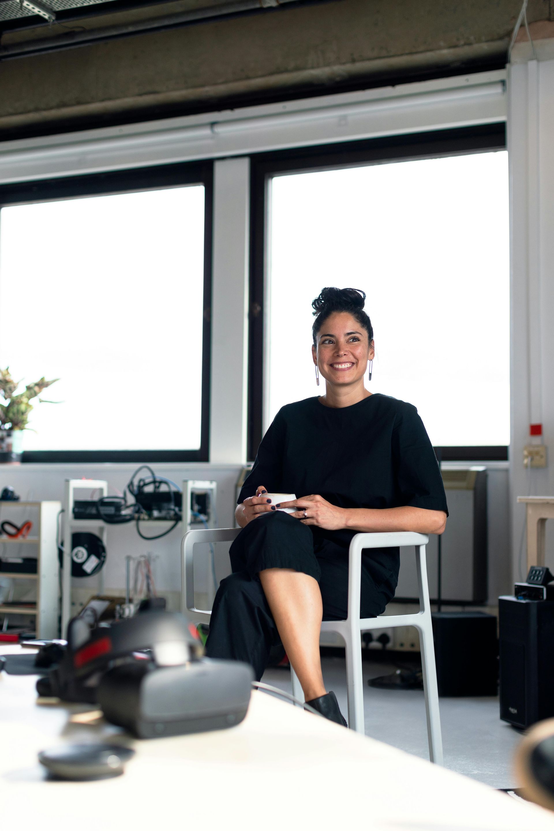 A woman in a black dress is sitting on a stool in front of a window.