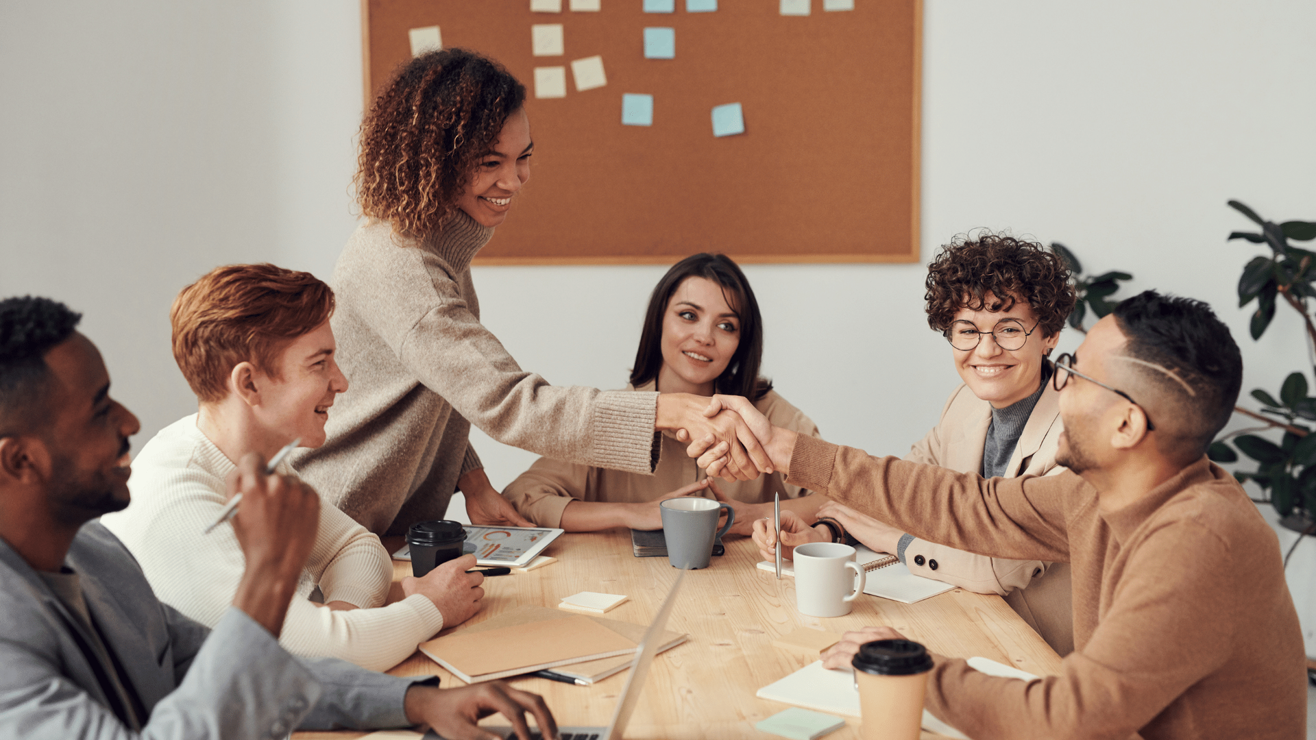 A group of people are sitting around a table shaking hands.