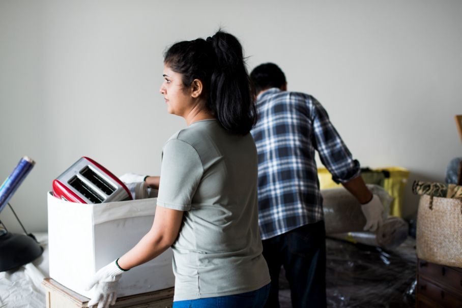 Woman and man carrying a box containing a toaster, in a room; moving.