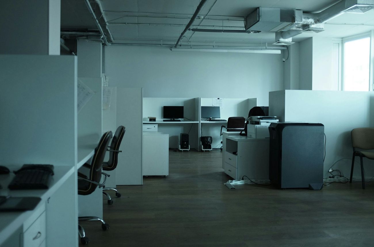 Empty modern office with desks, monitors, and chairs in a dimly lit open workspace