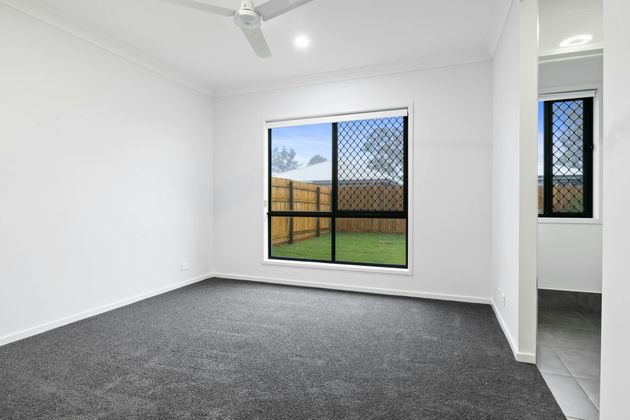 Empty white bedroom with gray carpet, large window, and open doorway to a tiled room.