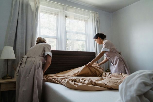 Two caregivers making a bed in a bright bedroom with white curtains