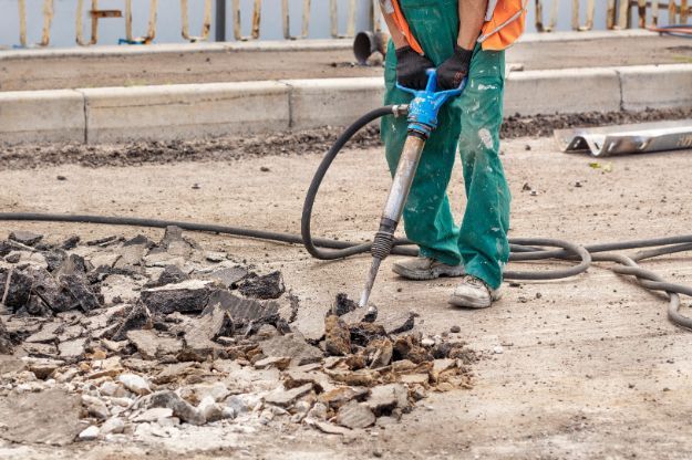 Construction worker using a jackhammer to break up asphalt on a road.