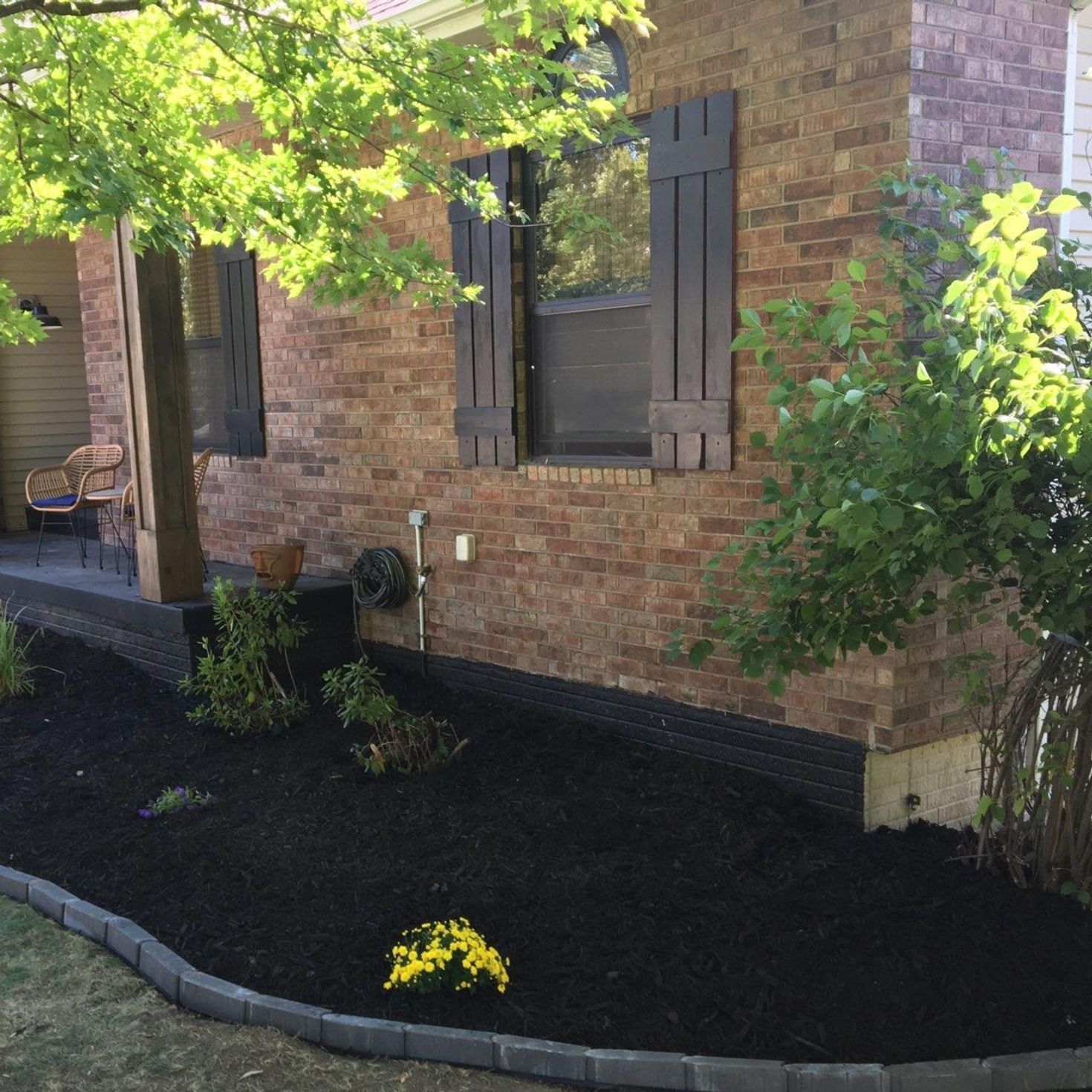 Landscaped flower bed with black mulch, edging, and house with brown shutters.