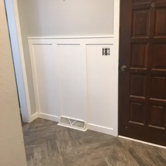 Interior hallway with white wainscoting, dark wood door, and a small wall vent near the floor
