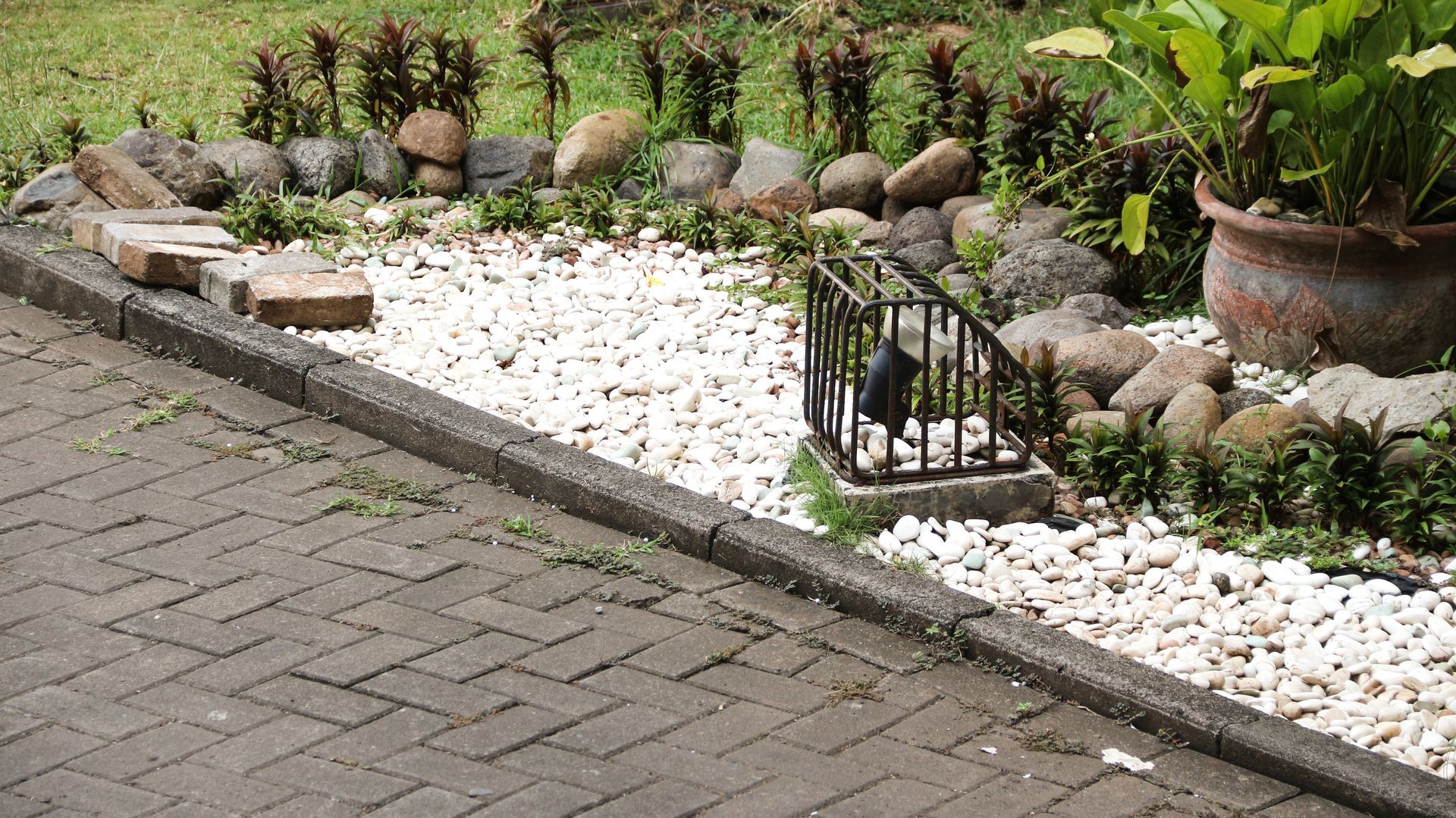 Brick paved path and garden bed with rocks, white pebbles, and plants.