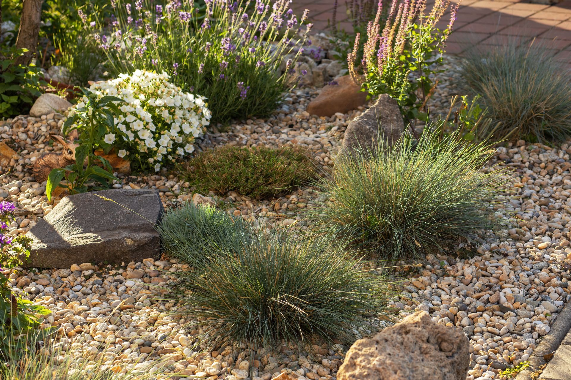 Rock garden with various green and purple plants, surrounded by gravel and stones.