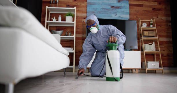 A man in a protective suit is spraying a room with a sprayer.