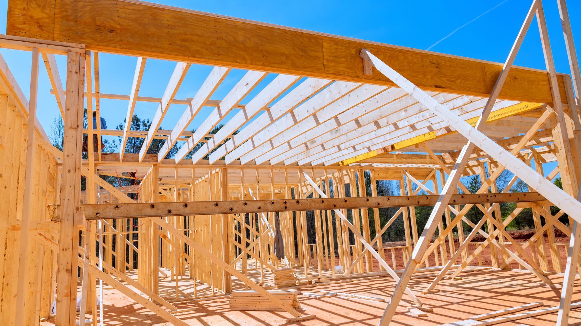 A house is being built with wooden beams and a blue sky in the background.