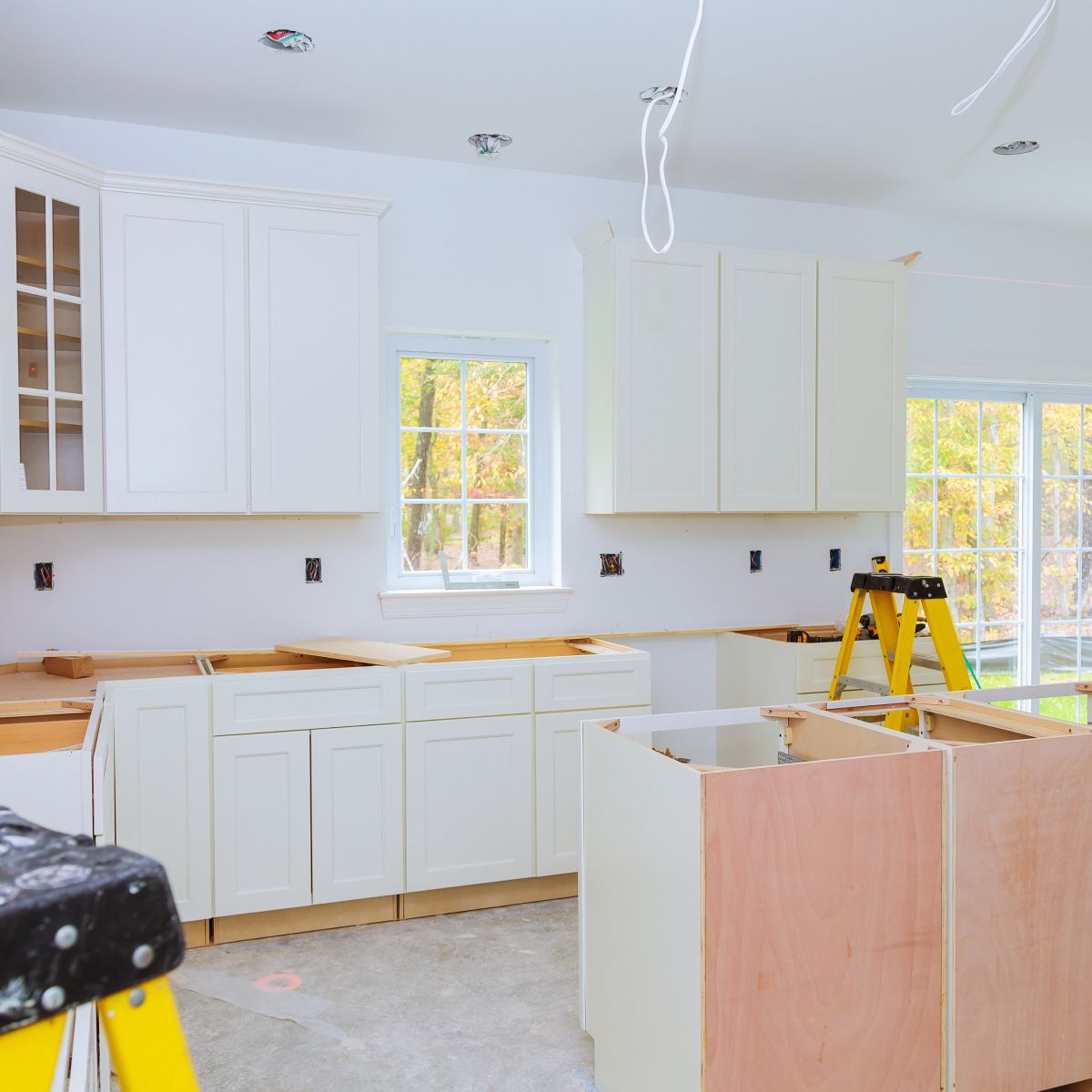 A kitchen under construction with white cabinets and a yellow ladder