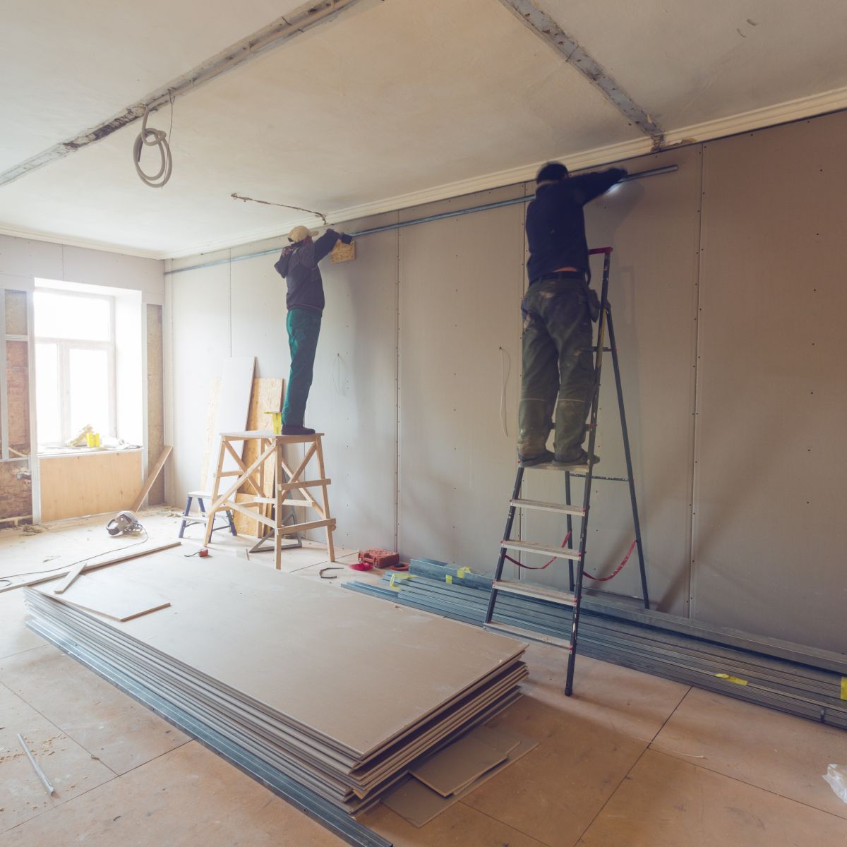 Two men are working on a wall in a room.