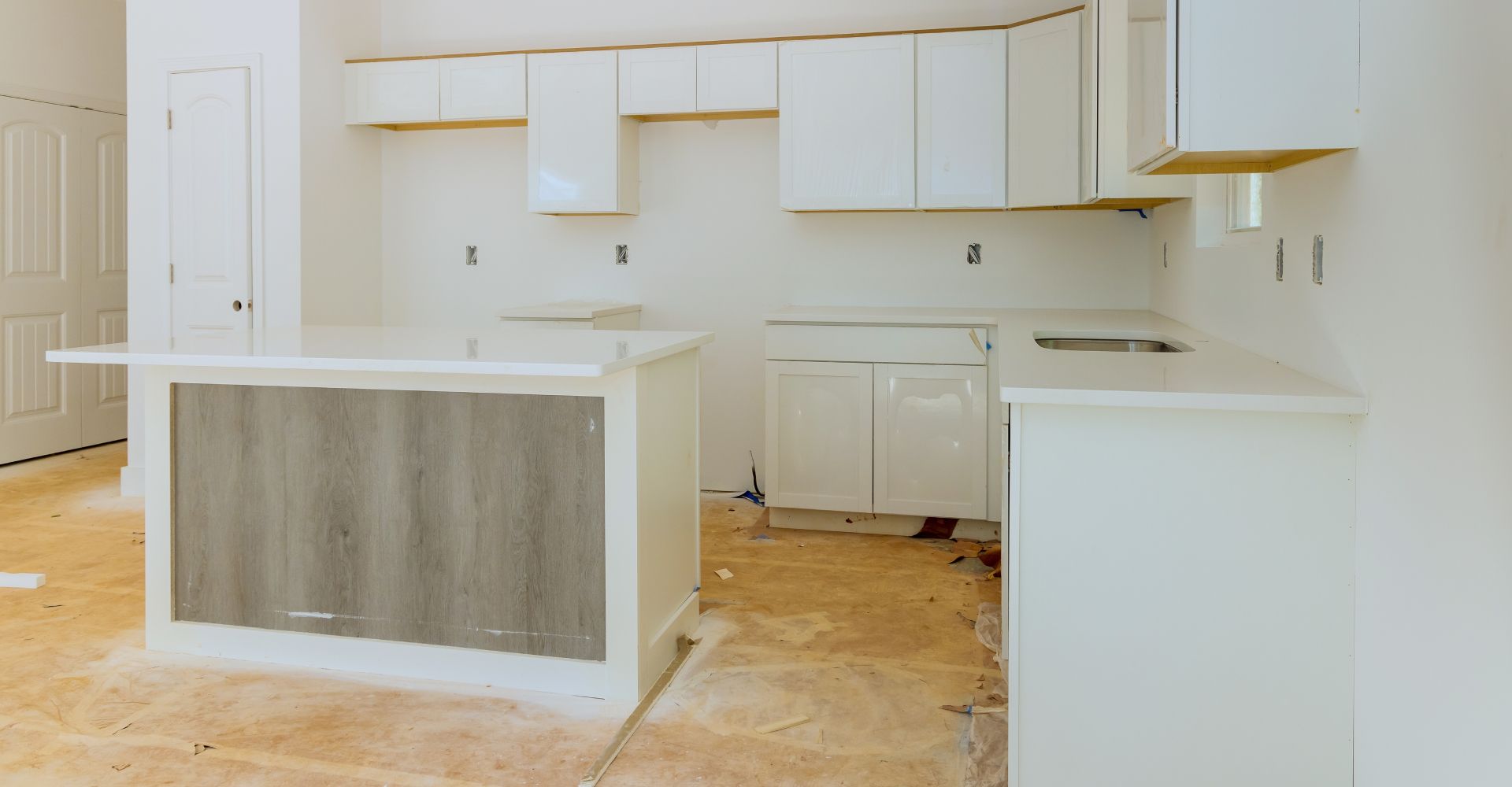 An empty kitchen with white cabinets and a wooden floor.