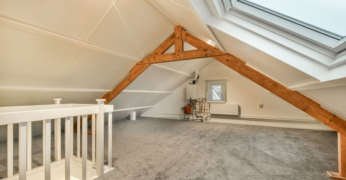 An empty attic with a skylight and wooden beams.