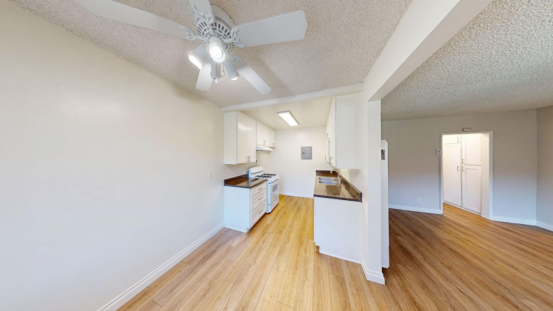 Interior view of a kitchen and dining area with white cabinets, wood floors, and ceiling fan.