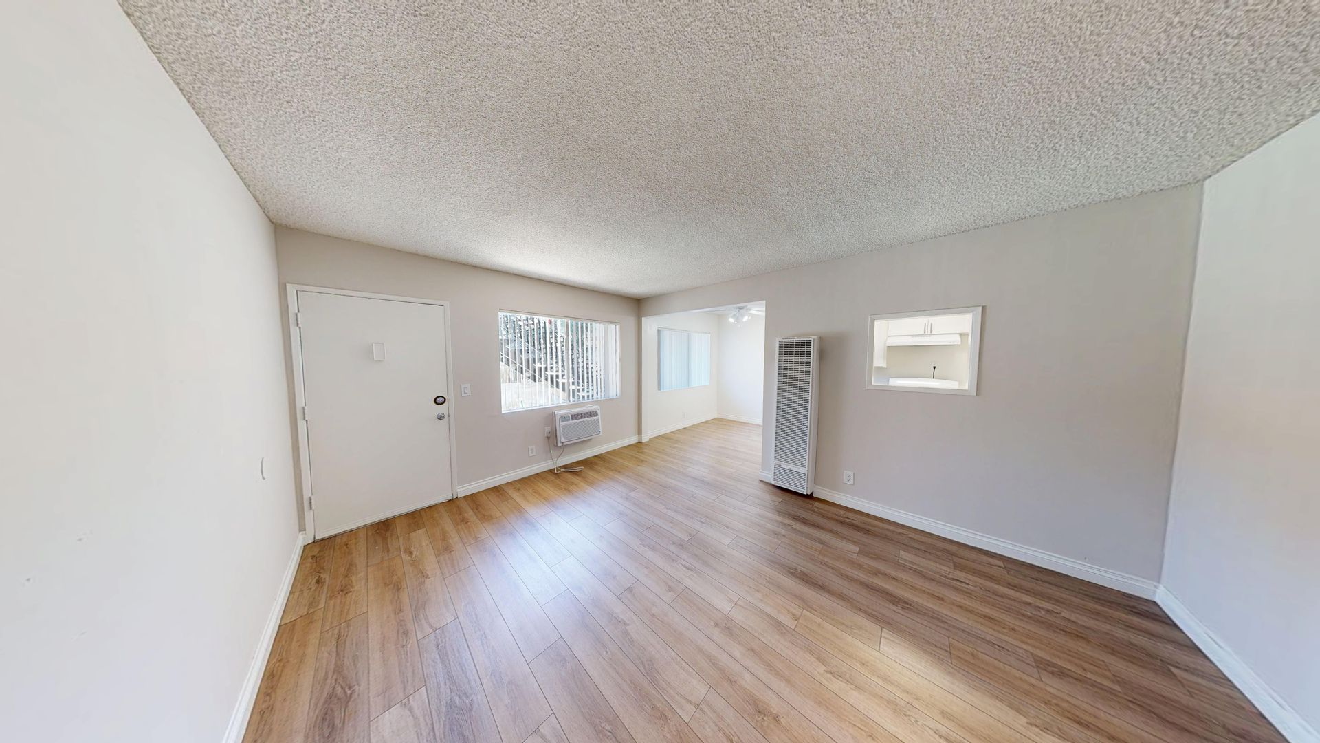 Interior apartment view with hardwood floors, white walls, and a window.