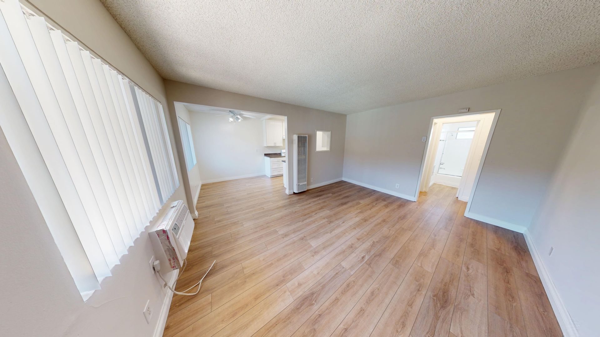 Interior view of an apartment with hardwood floors, a kitchen in the distance, and a bathroom doorway.