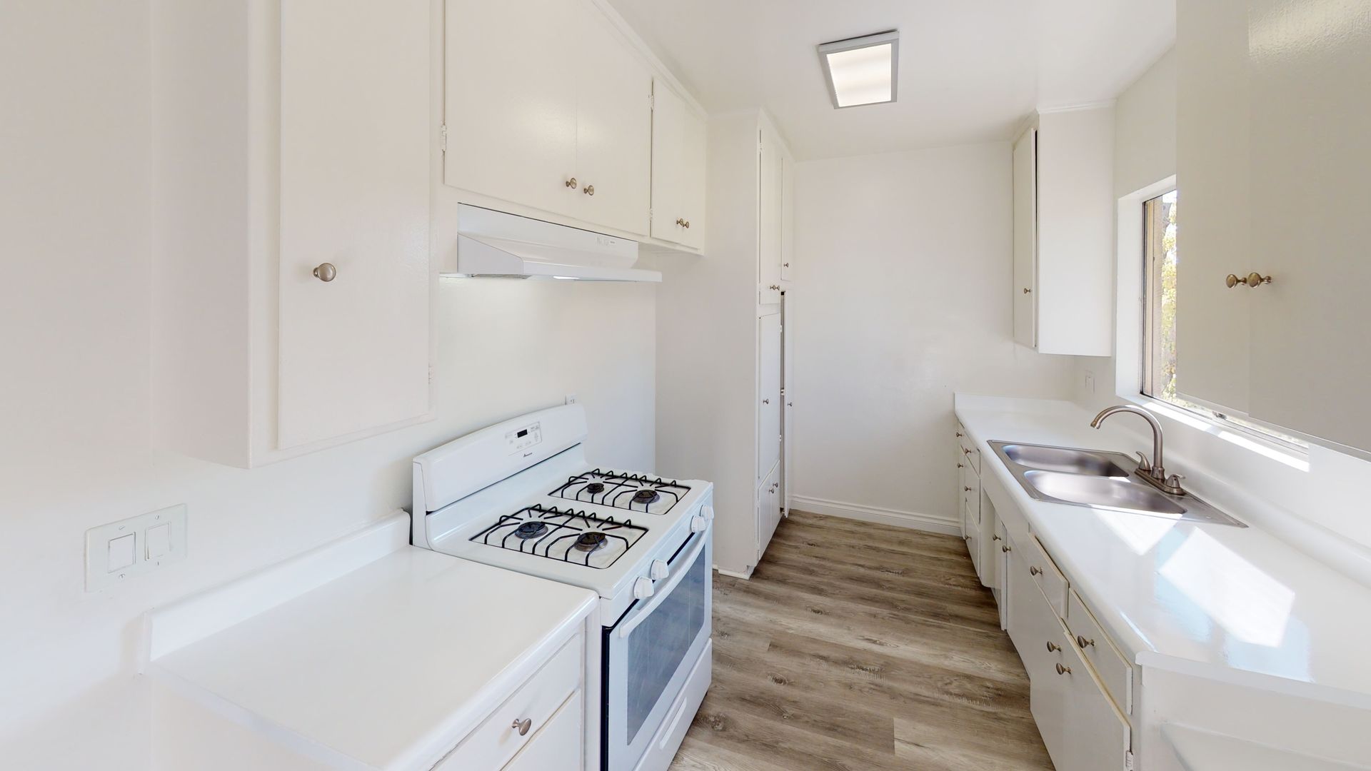 White kitchen with stove, cabinets, sink, and light wood-look flooring.
