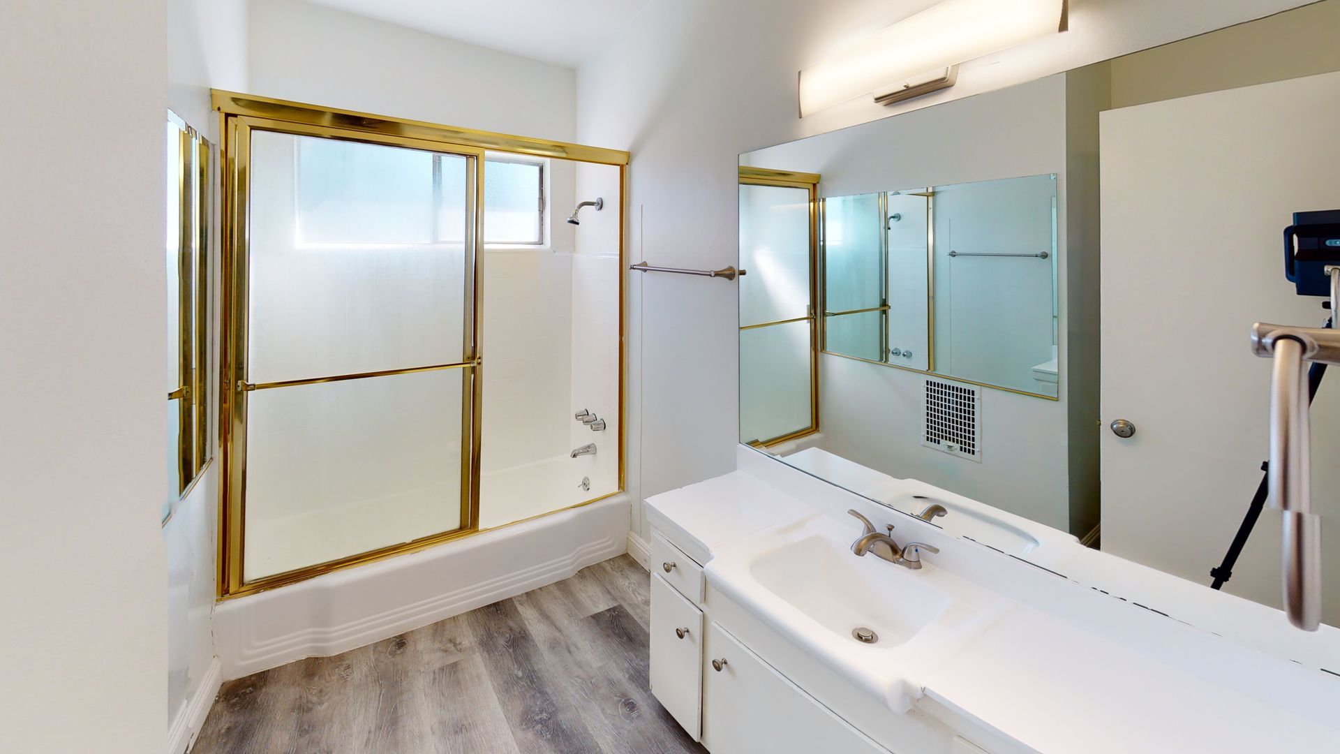 Bathroom with a white vanity and shower/tub combo with gold trim. Gray wood-look floor.