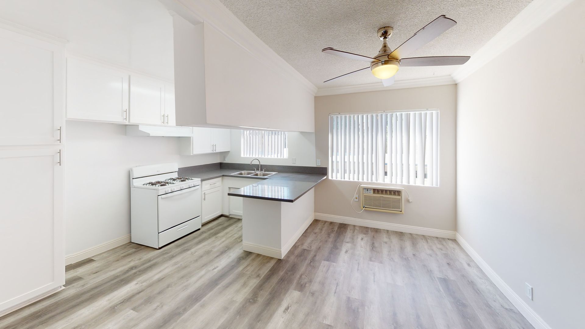 Kitchen with white cabinets, stove, and light gray countertops, next to a window with blinds.