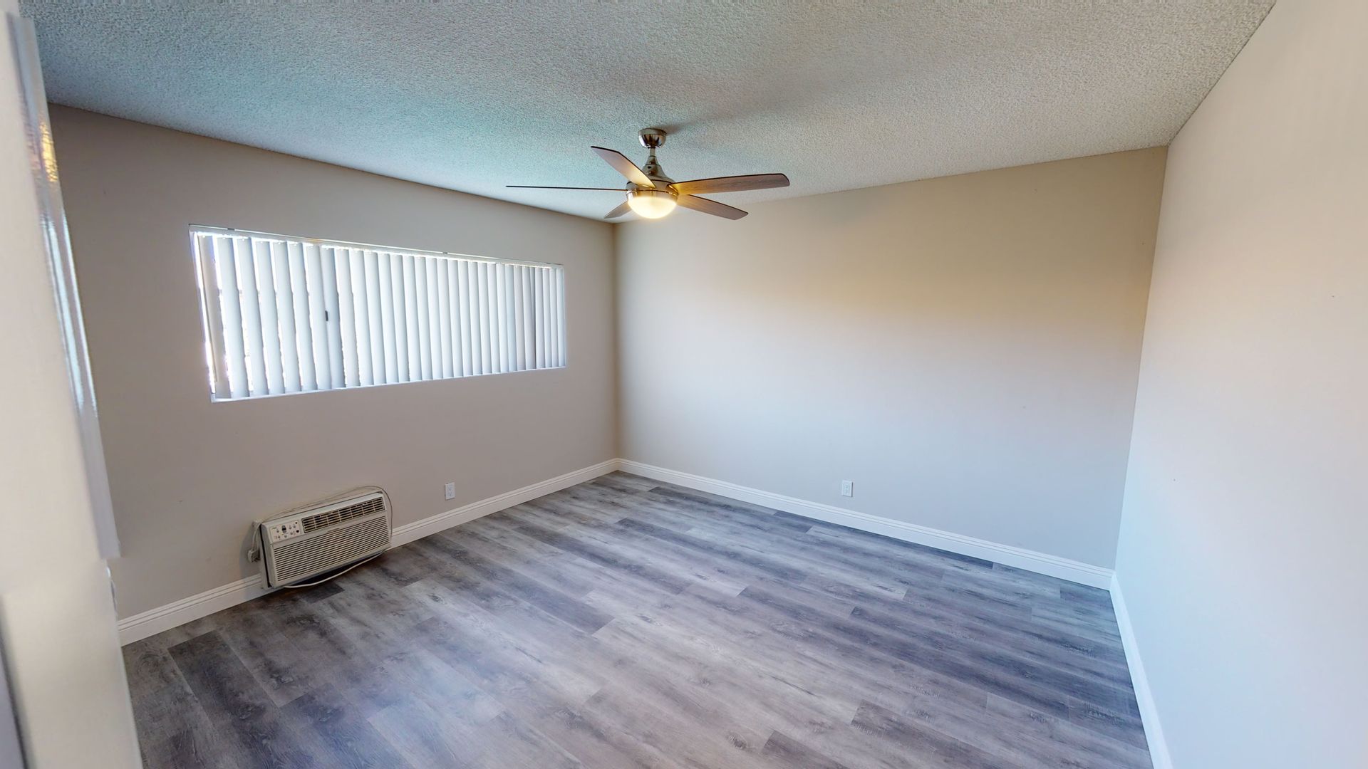 Empty room with light gray walls, wood-look flooring, ceiling fan, and window with blinds.
