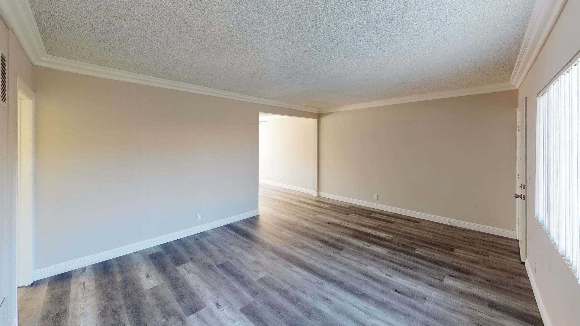 Empty room with gray wood-look flooring, beige walls, white trim and ceiling. Doorway on the left.