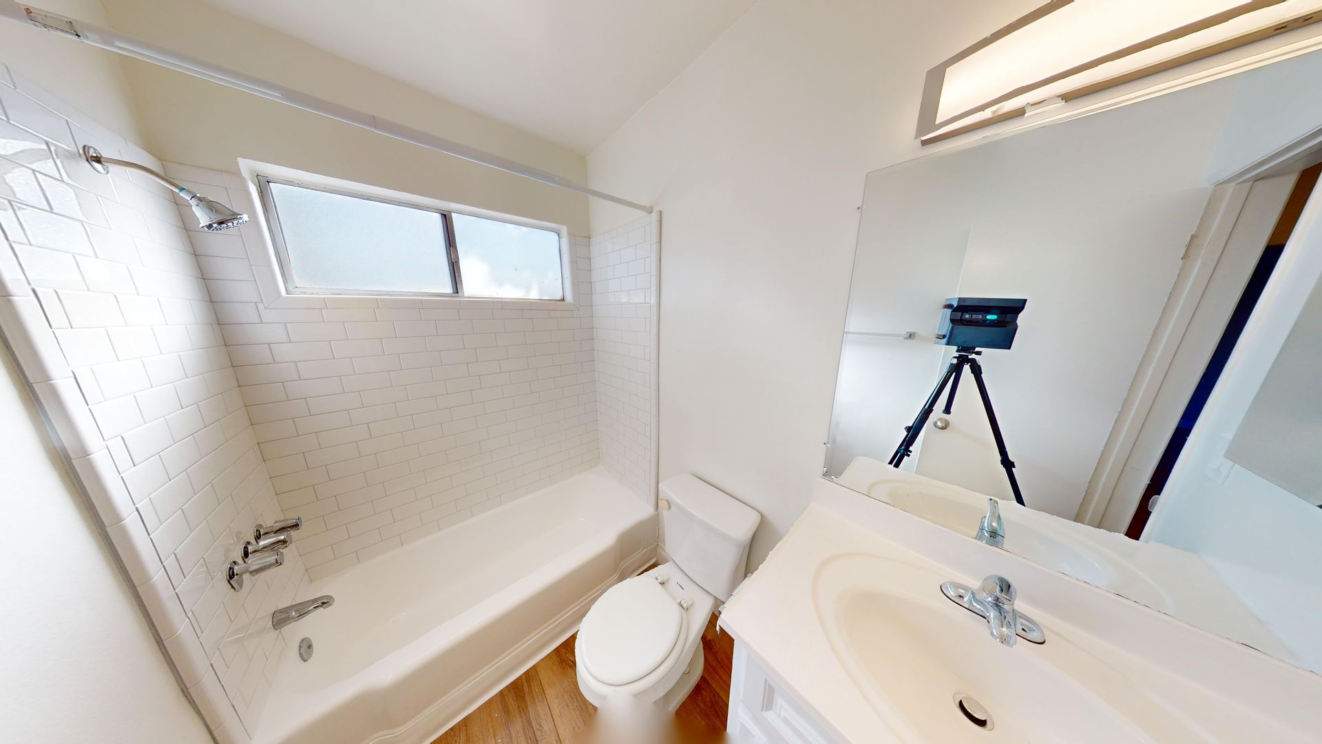 Bathroom with tub, toilet, and vanity. White walls and fixtures. Tripod with camera in mirror.