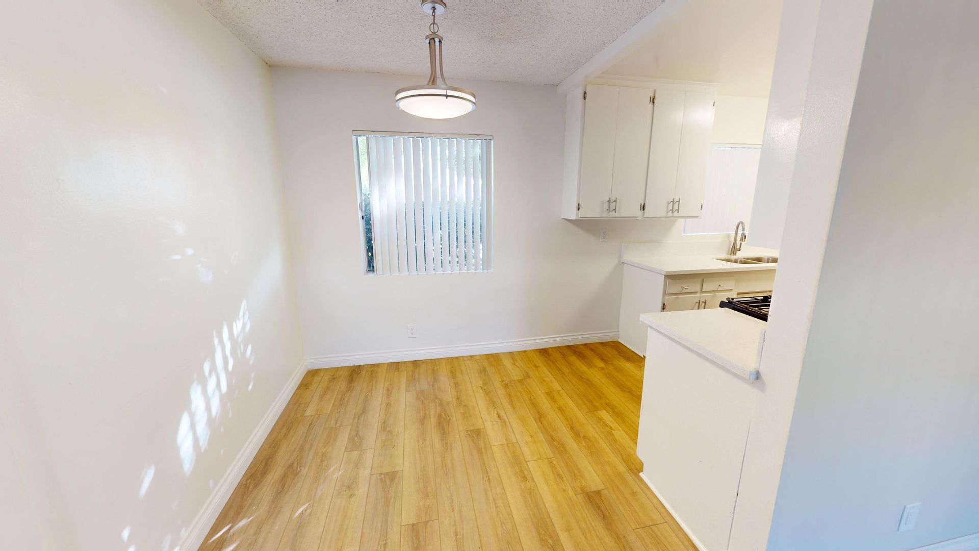 Empty dining room with wood flooring, white walls, and a small kitchen visible.