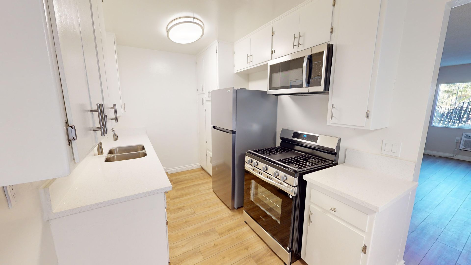 Kitchen with white cabinets, stainless steel appliances, and wood-look flooring.