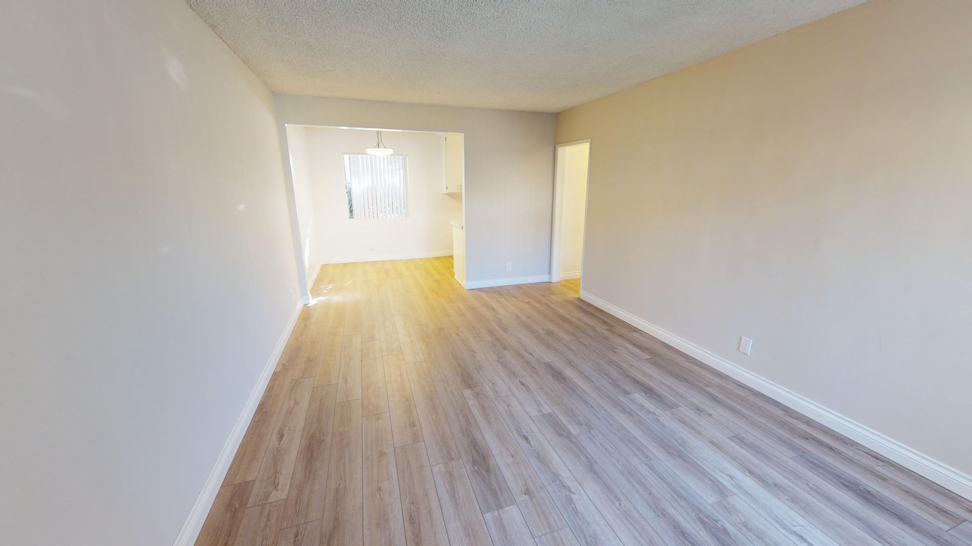Empty room with light wood-look flooring and white walls, leading to other rooms.